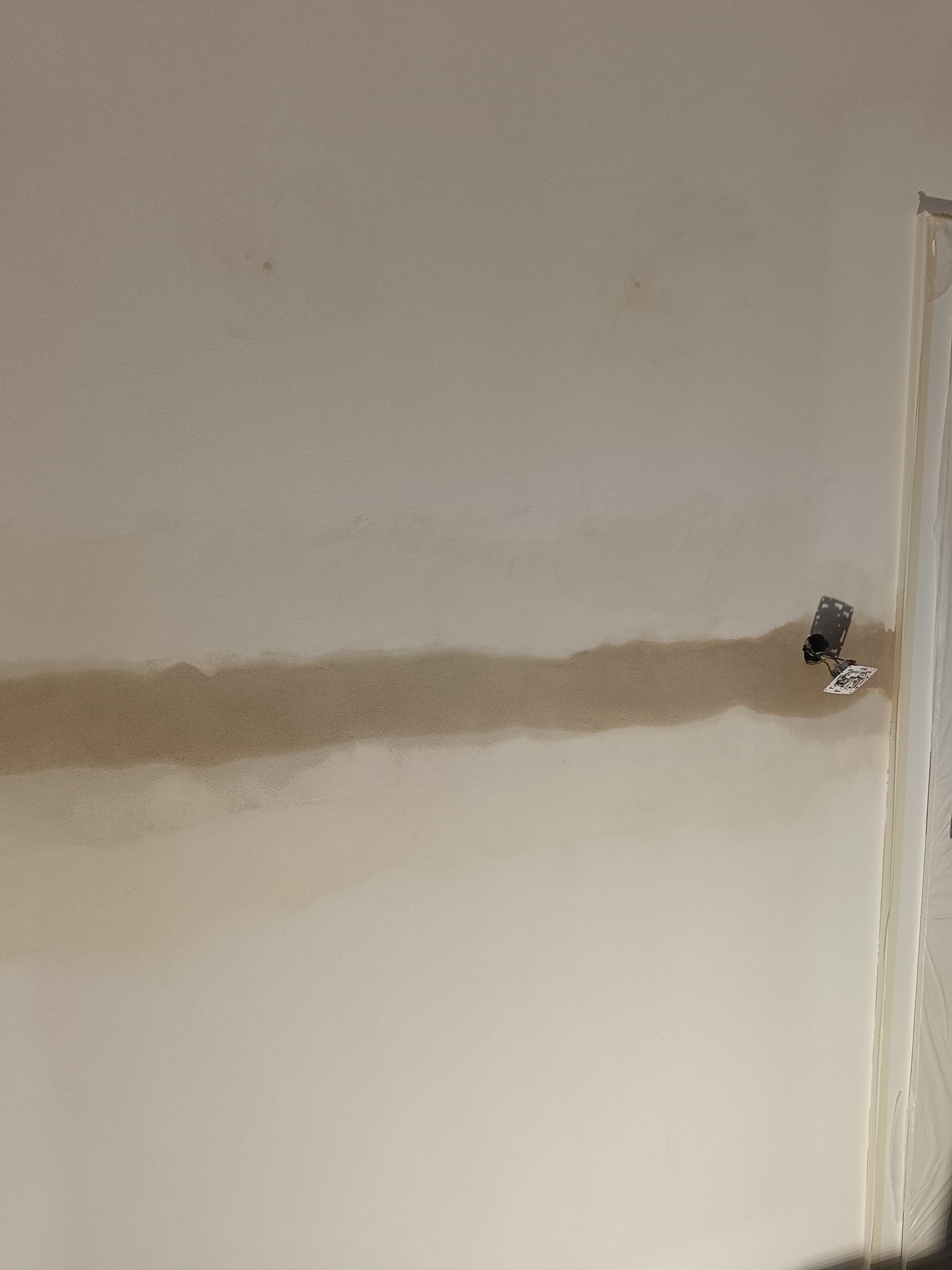 Ściana w trakcie prac przygotowawczych: widoczna warstwa szpachli nałożona w poziomie, z zamontowanym gniazdkiem elektrycznym. Fragment folii ochronnej przy framudze drzwi.