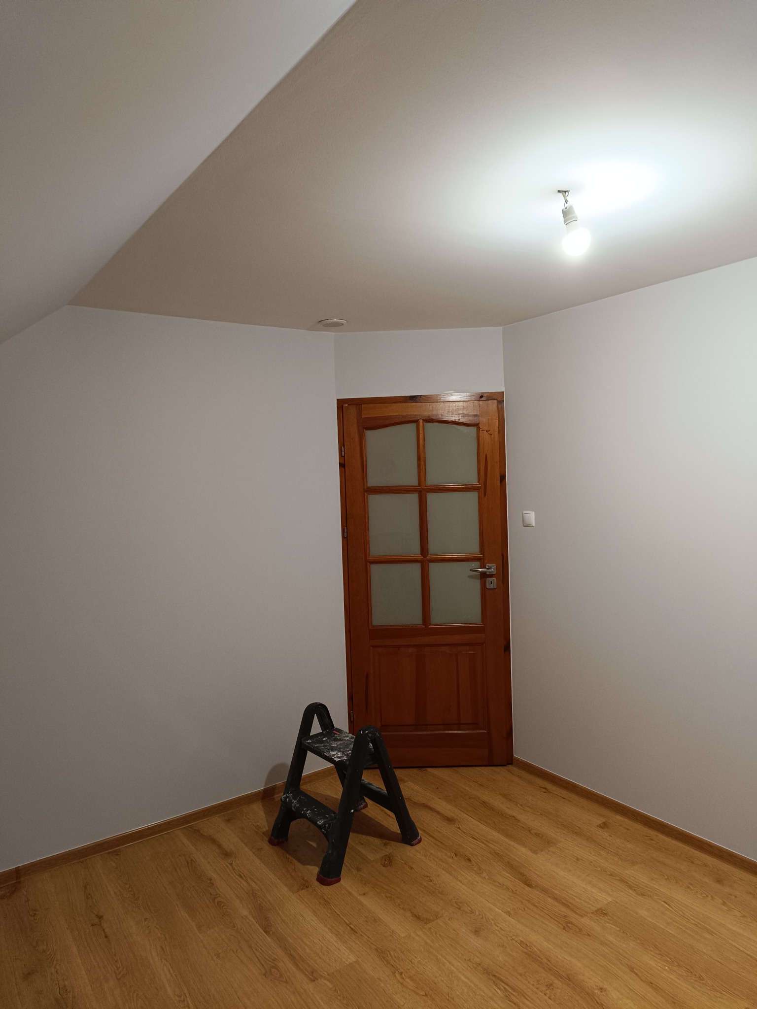 Wnętrze pokoju po świeżym pomalowaniu na biało, widoczna drabinka malarska, drewniana podłoga i drzwi z szybami.