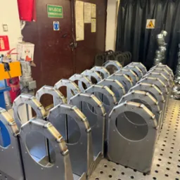 Szereg identycznych, spawanych konstrukcji metalowych z okrągłym otworem, ustawionych na perforowanym stole spawalniczym w warsztacie. Widoczne spoiny i elementy mocujące.