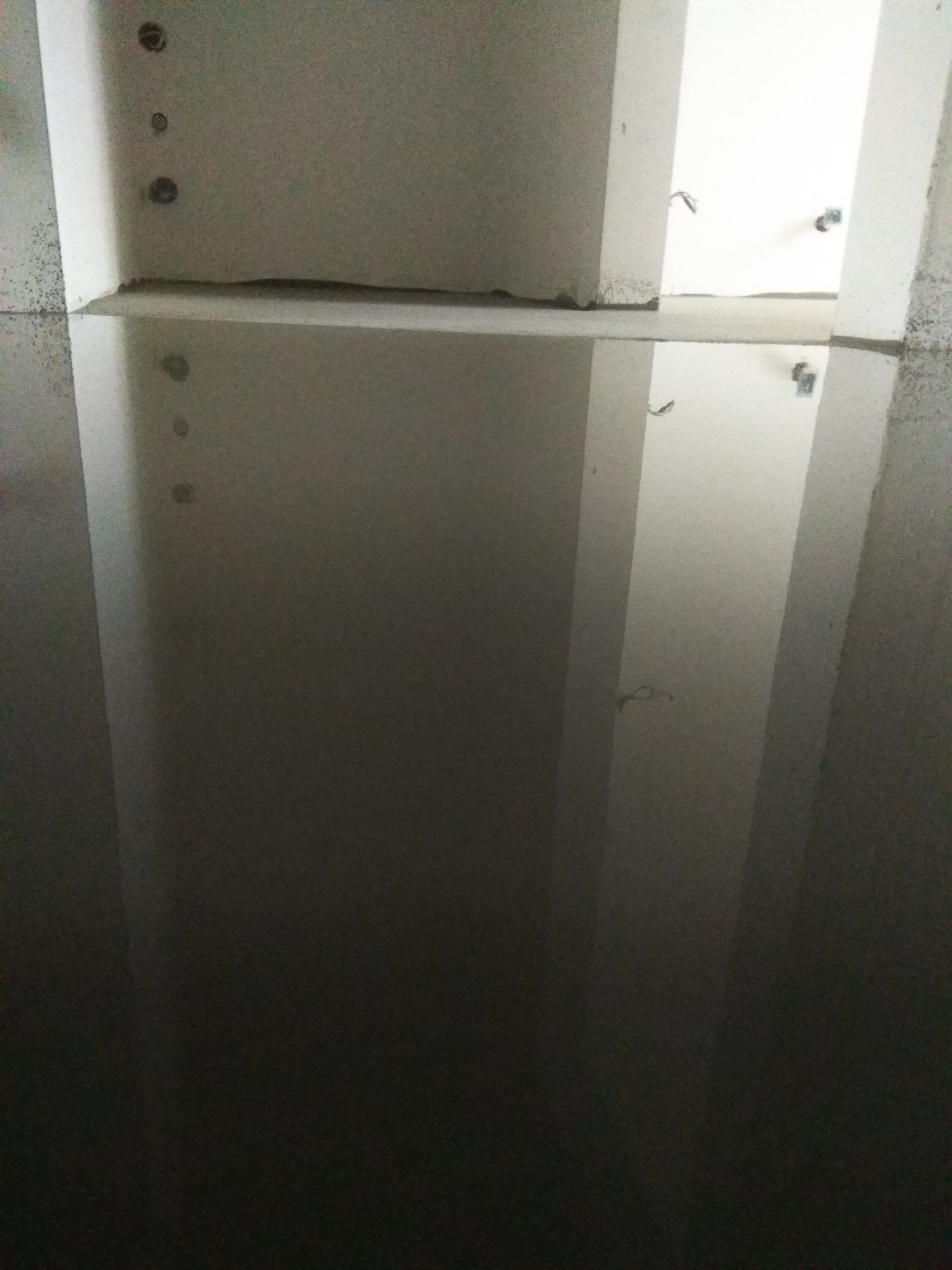 Surowy stan ścian i sufitu w trakcie prac budowlanych, widoczne otwory montażowe i przewody elektryczne wystające ze ściany.