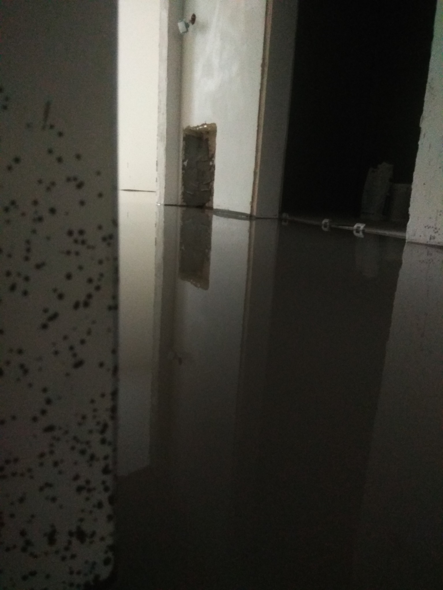 Świeżo wylana, gładka posadzka jastrychowa w trakcie schnięcia, widoczne ślady po narzędziach i poziomice, ściany w surowym stanie, przygotowane do dalszych prac.