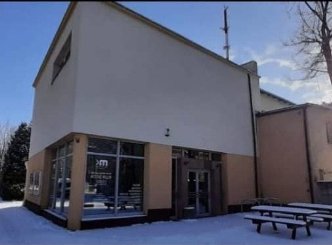 Nowoczesny budynek biurowy z płaskim dachem i dużymi oknami, zimowy krajobraz z zaspami śnieżnymi, widoczny fragment elewacji i wejście.