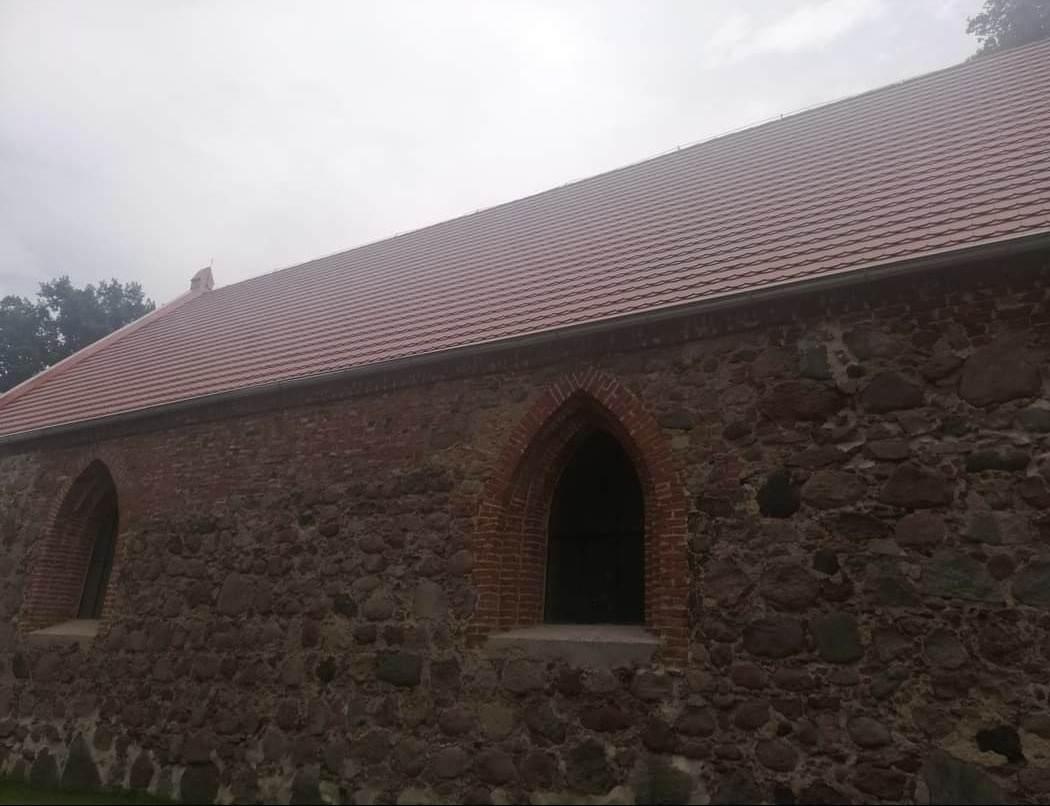 Odnowiony budynek z kamienno-ceglaną elewacją, z nową czerwoną dachówką i gotyckimi oknami w ceglanych obramowaniach.