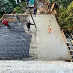 Motex - Wylewka betonu na zbrojenie stropu z użyciem pompy, widoczne pręty zbrojeniowe i pracownicy. Częściowo zalana powierzchnia. Ujęcie z góry.