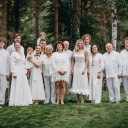 Ewelina Kwiatek- Fotografia - Duża grupa ludzi ubranych na biało pozuje na trawniku przed lasem, różnorodne style ubioru i wieku, uśmiechnięte twarze, swobodna atmosfera.