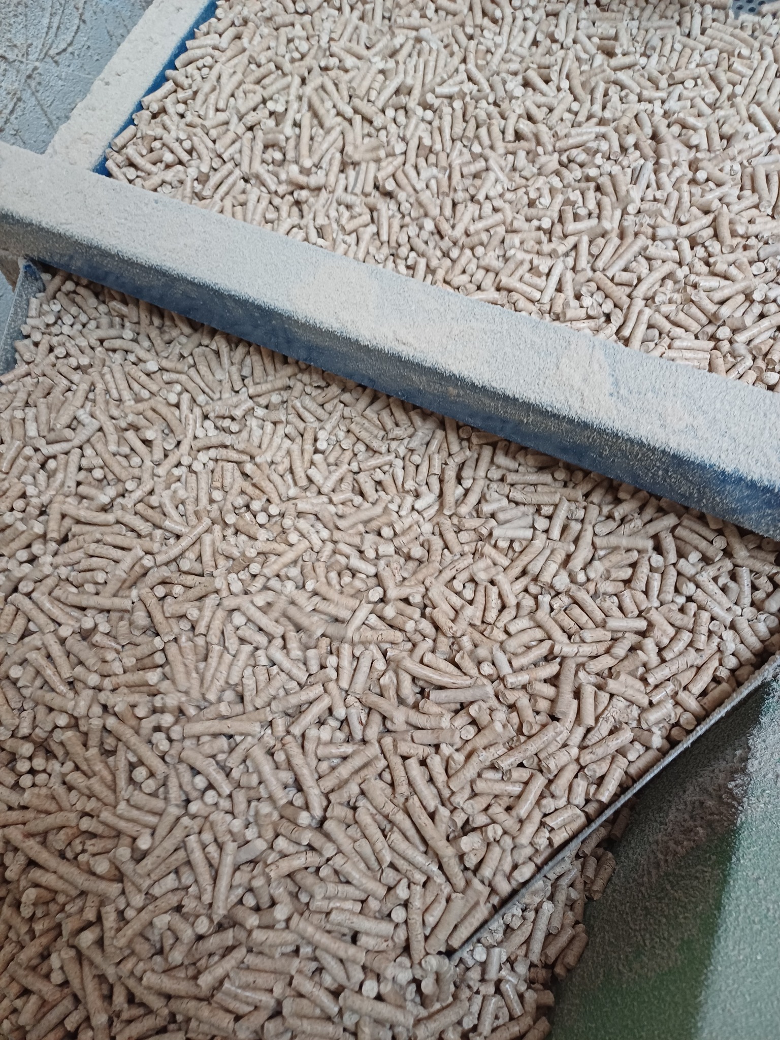 Dwa pojemniki wypełnione pelletem drzewnym, z widocznym pyłem na krawędziach metalowych konstrukcji.