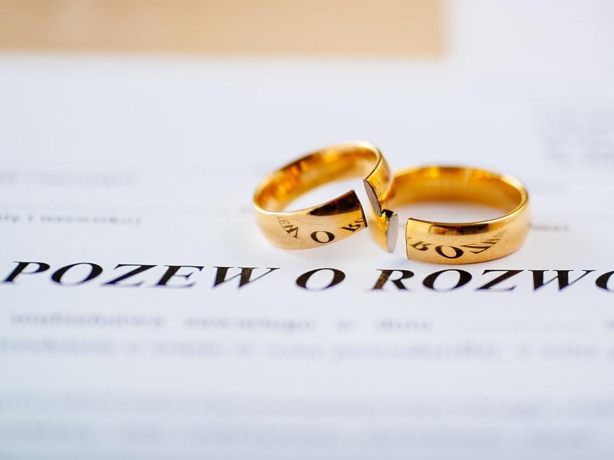 Dwa złote, pęknięte obrączki leżące na dokumencie z napisem 'POZEW O ROZWÓD'.