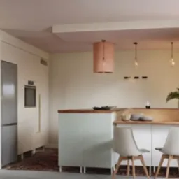 Jasna kuchnia z wyspą i dwoma krzesłami w stylu skandynawskim, różowy sufit, minimalistyczne lampy wiszące i roślina doniczkowa.