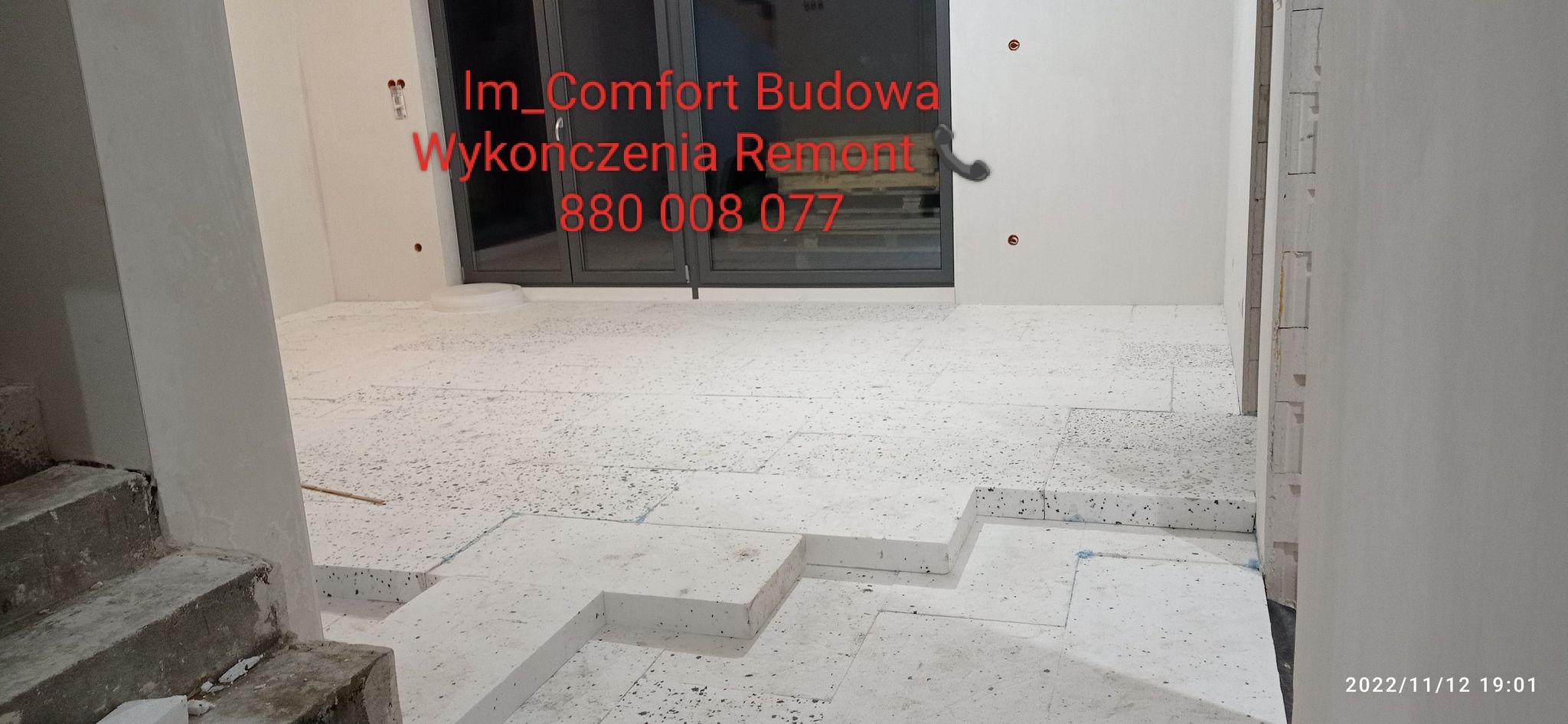 Białe płyty styropianowe ułożone na podłodze w trakcie prac przygotowawczych do remontu, widoczne schody w surowym stanie i okno balkonowe w tle.