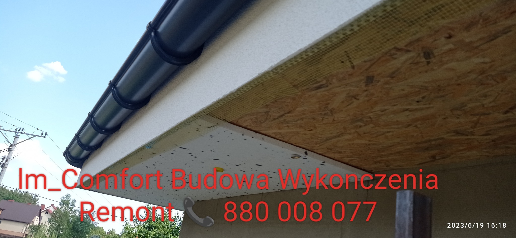 Widok z dołu na fragment ocieplonej elewacji z zamontowaną czarną rynną, widoczna warstwa izolacyjna i deska OSB. Na zdjęciu widoczny jest również numer telefonu firmy budowlanej.