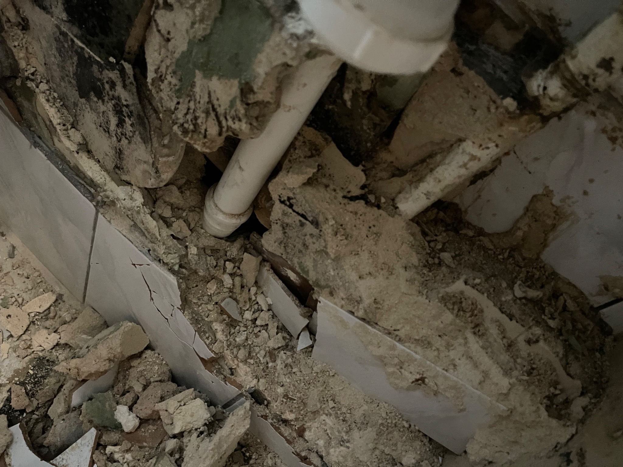 Zdemolowany fragment ściany z widocznymi rurami i gruzem, wskazujący na etap prac przygotowawczych do remontu łazienki.