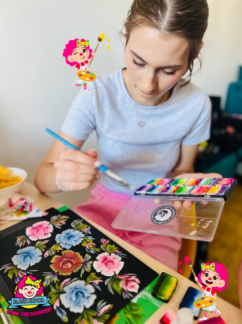 Młoda kobieta maluje kwiaty akwarelą na czarnym papierze, używając pędzla i palety z farbami, z naklejkami klauna w rogach.
