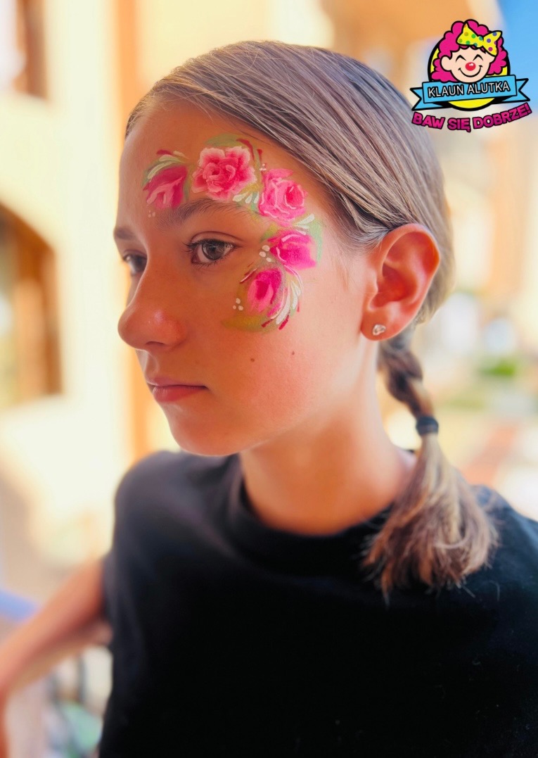 Dziewczynka z pomalowaną twarzą w motywy różowych róż i zielonych liści, profil, w tle logo firmy animatora.