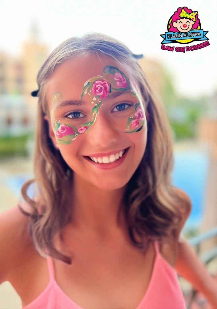 Uśmiechnięta nastolatka z artystycznym malunkiem na twarzy przedstawiającym różowe róże i zielone pnącza, logo firmy widoczne w górnym rogu.