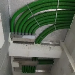 Zielone, karbowane rury wentylacyjne zamontowane pod sufitem z izolacją termiczną, przymocowane metalowymi opaskami.