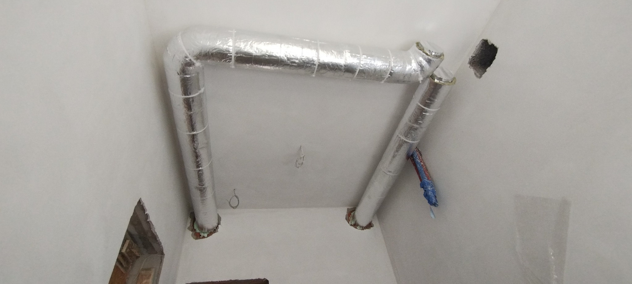 System kanałów wentylacyjnych z izolacją aluminiową, zamontowany pod sufitem w pomieszczeniu w trakcie remontu, widoczne otwory w ścianach i wystające przewody.