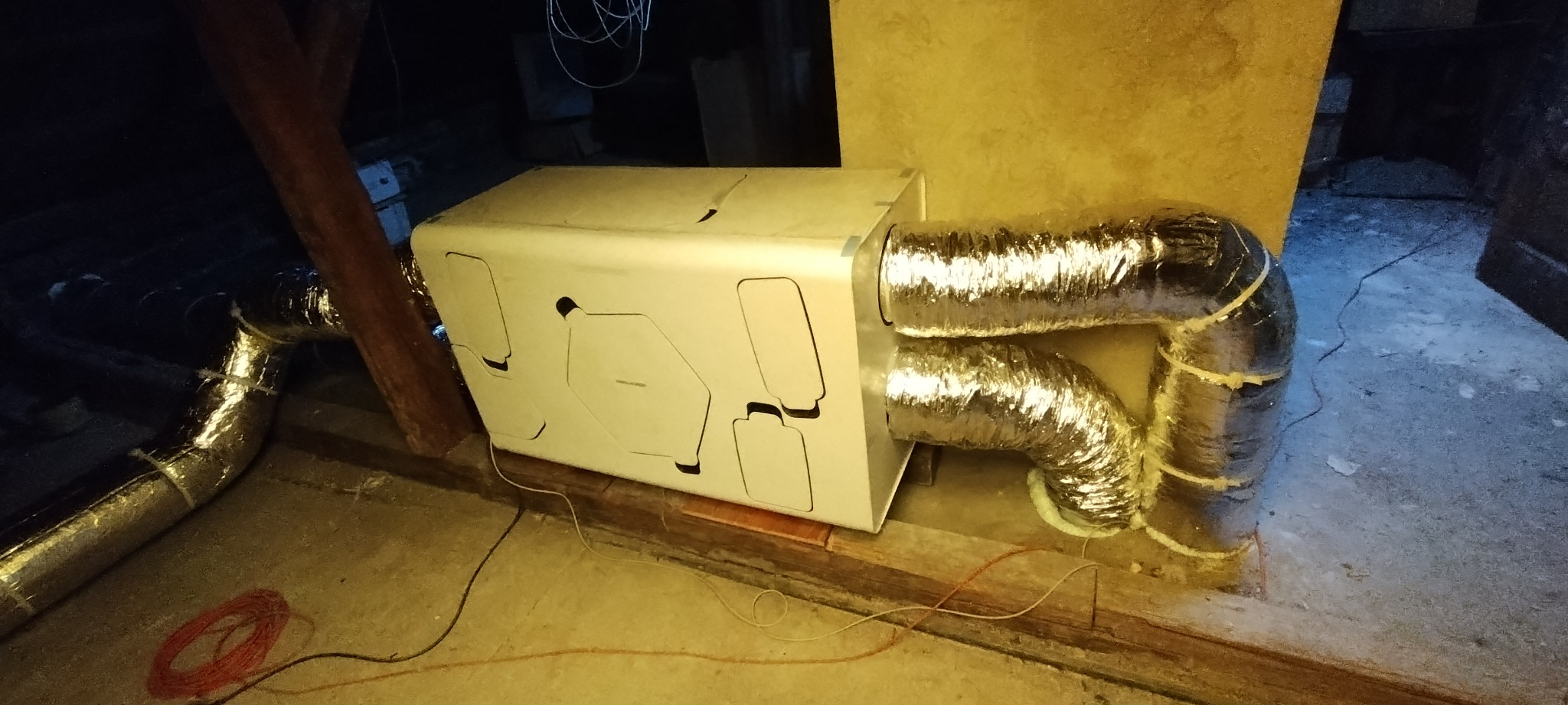 Centrala wentylacyjna z rekuperacją zamontowana na poddaszu, widoczne srebrne rury wentylacyjne i drewniane elementy konstrukcyjne dachu.