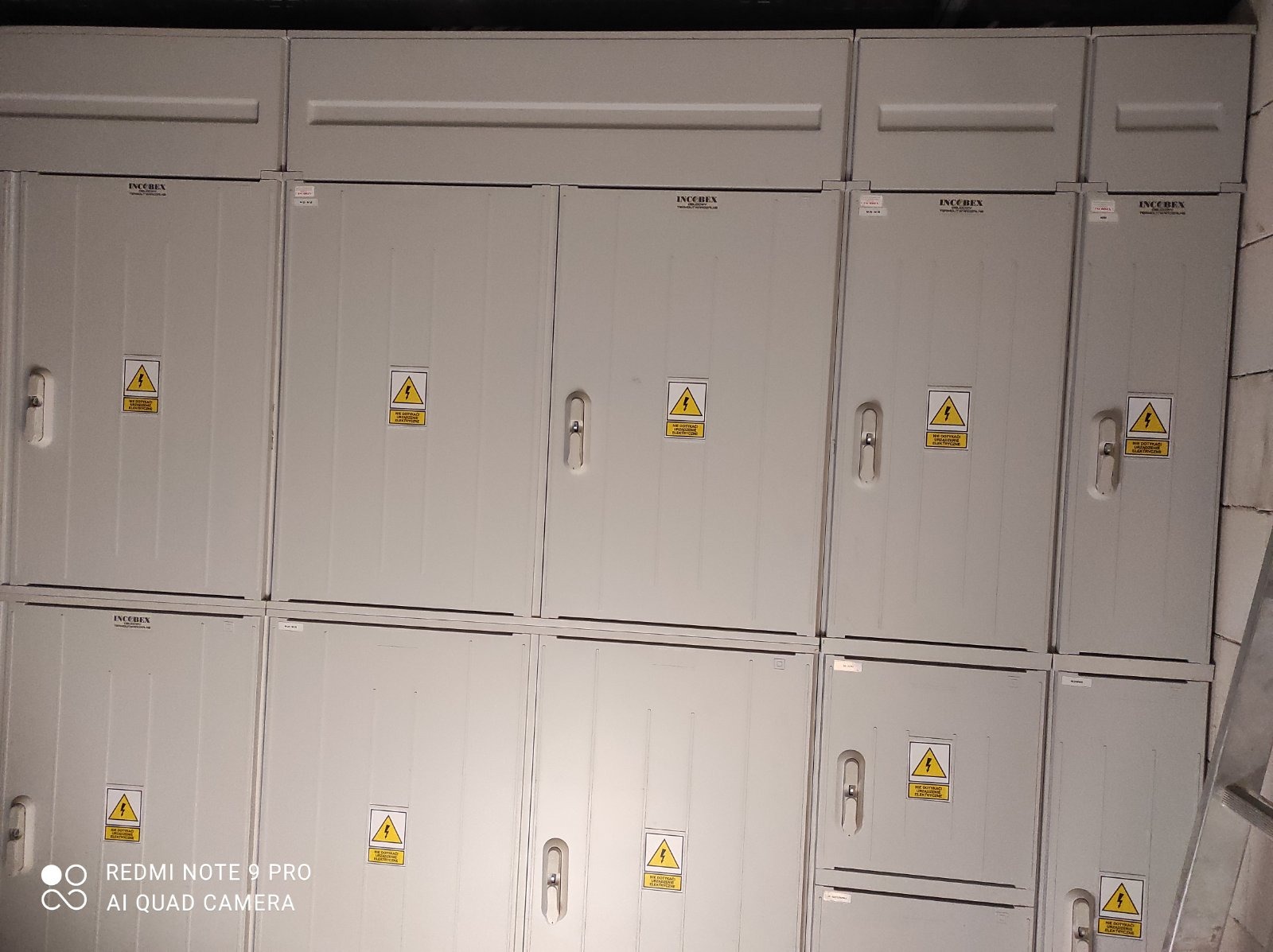 Rozbudowana tablica elektryczna z wieloma szarymi szafkami z ostrzeżeniami o napięciu, widok z dołu z lekkim kątem