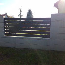 DK STAL Daniel Kaleta - Nowoczesne ogrodzenie panelowe z elementami betonowymi i metalowymi, widok z zewnątrz na tle trawnika i zabudowań.