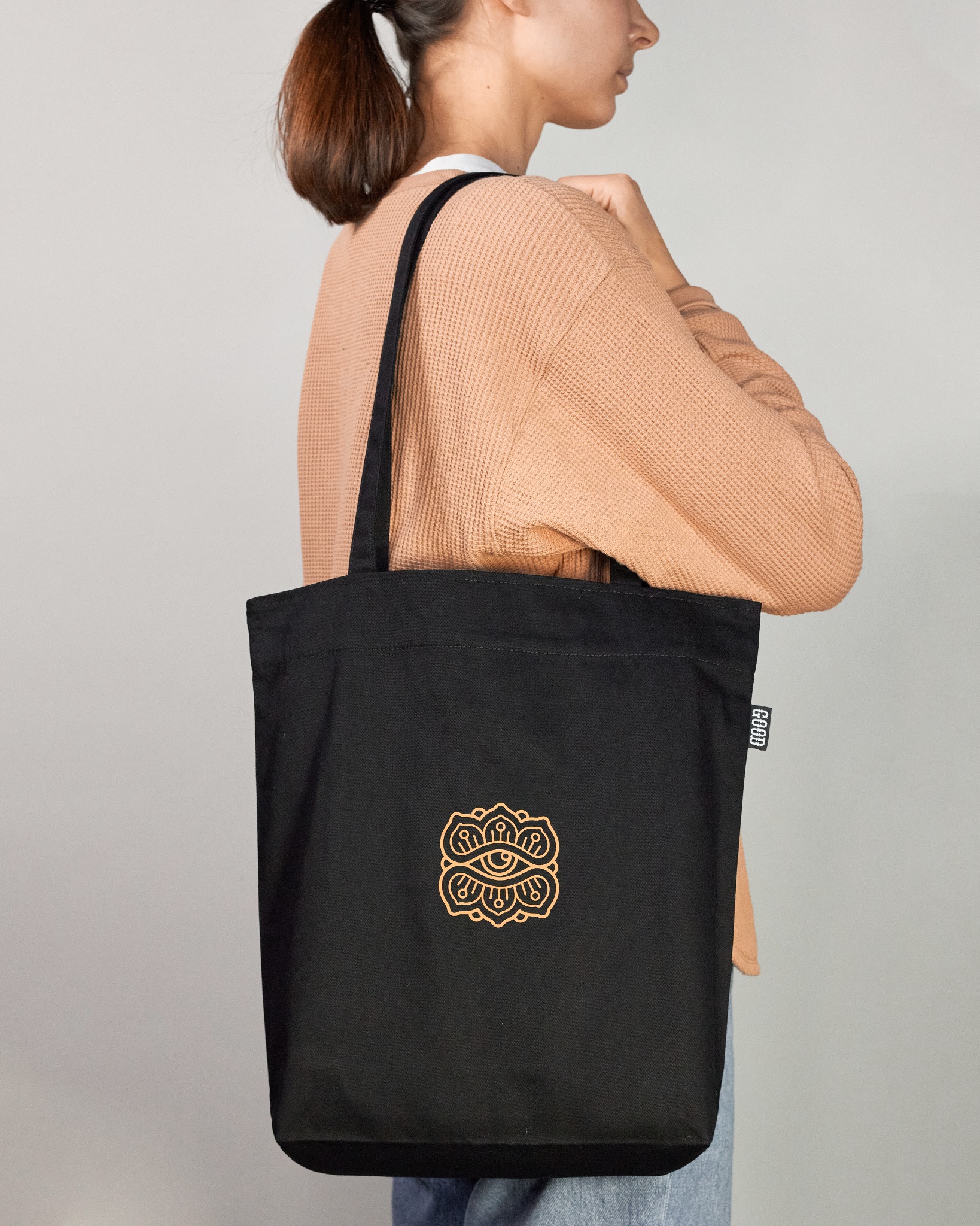 Czarna torba bawełniana z nadrukiem graficznym w kolorze złotym, prezentowana na ramieniu osoby w beżowym swetrze.