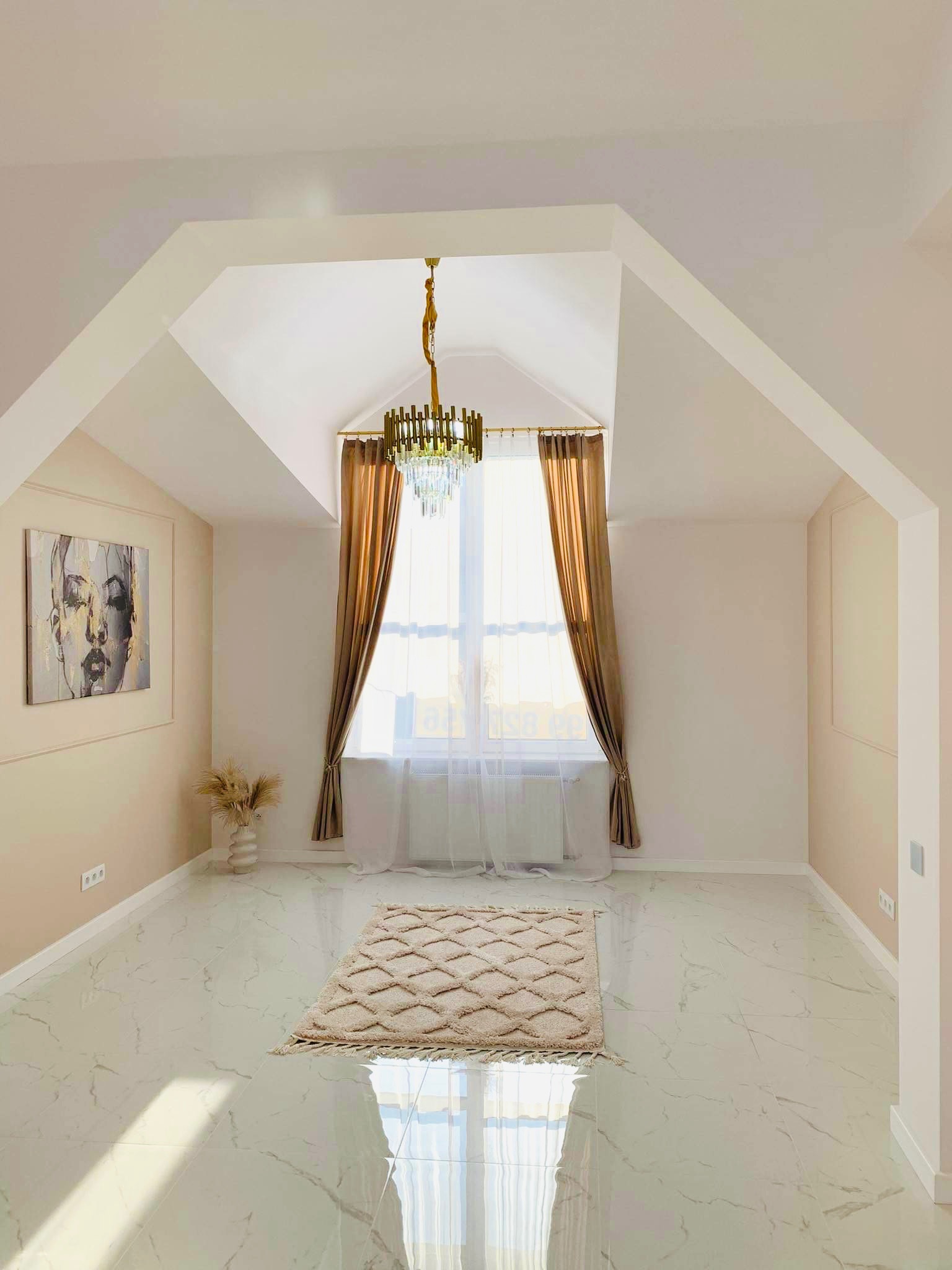 Jasne poddasze z marmurową podłogą, beżowymi ścianami z dekoracyjnymi listwami, obrazem kobiety, dywanem w geometryczne wzory i kryształowym żyrandolem, oświetlone naturalnym światłem wpadającym...