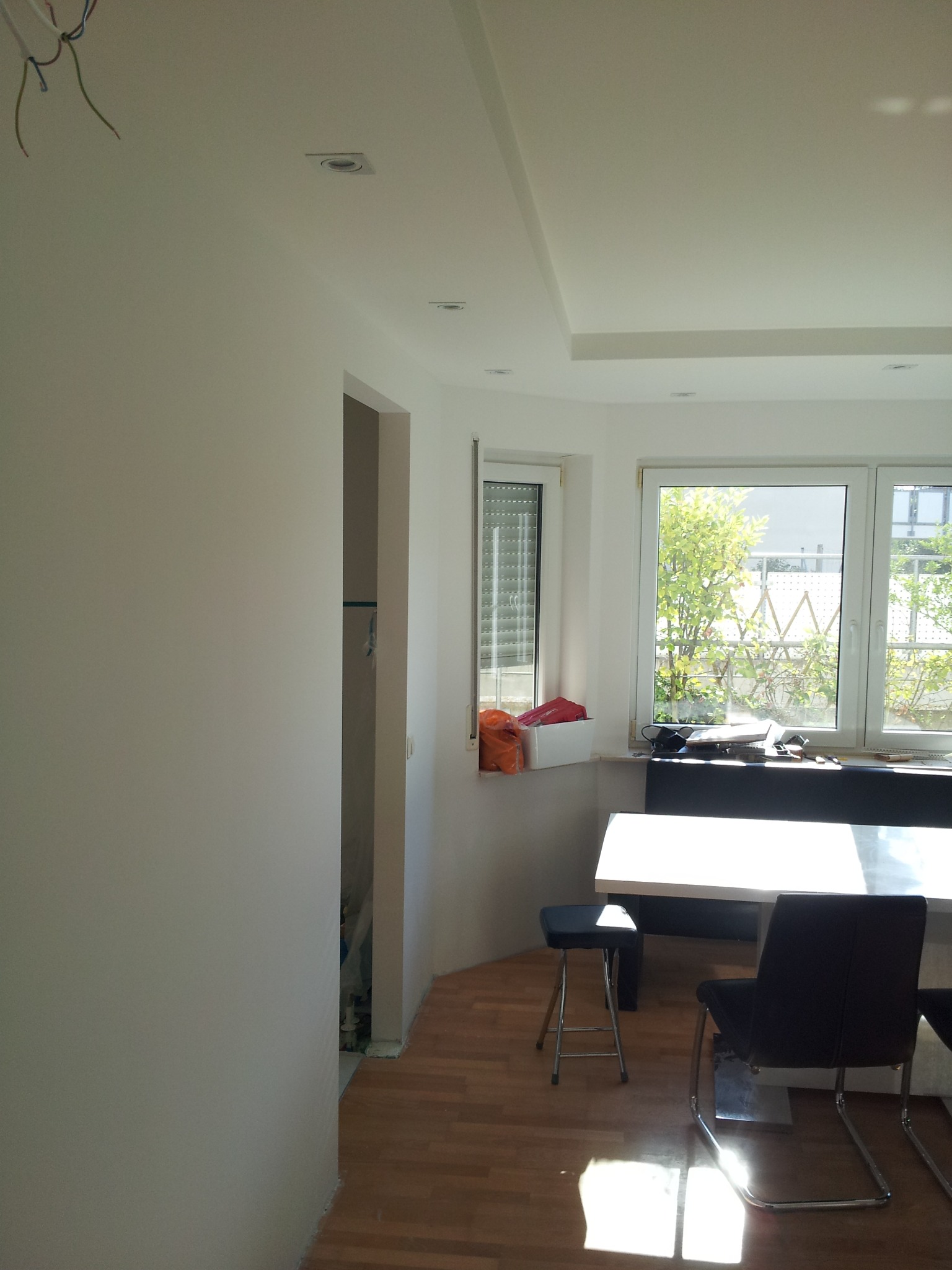 Jasne wnętrze pokoju po malowaniu ścian na biało, widoczne gładkie ściany, parkiet na podłodze, okno z widokiem na zieleń, oraz minimalistyczne meble.