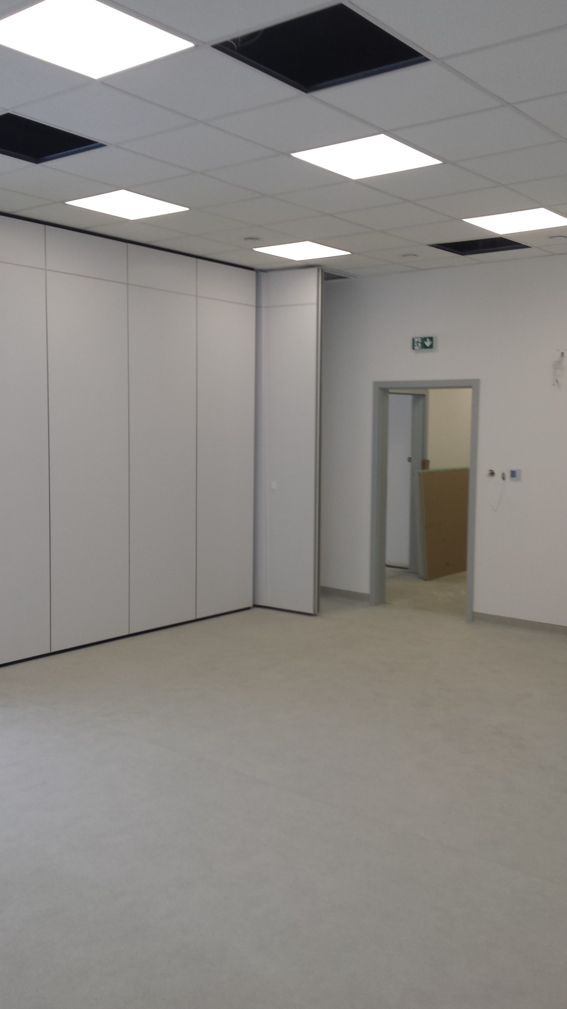 Białe, przesuwne ściany działowe w jasnym, nowym biurze z podwieszanym sufitem i panelami LED, widok na otwarte drzwi do sąsiedniego pomieszczenia.