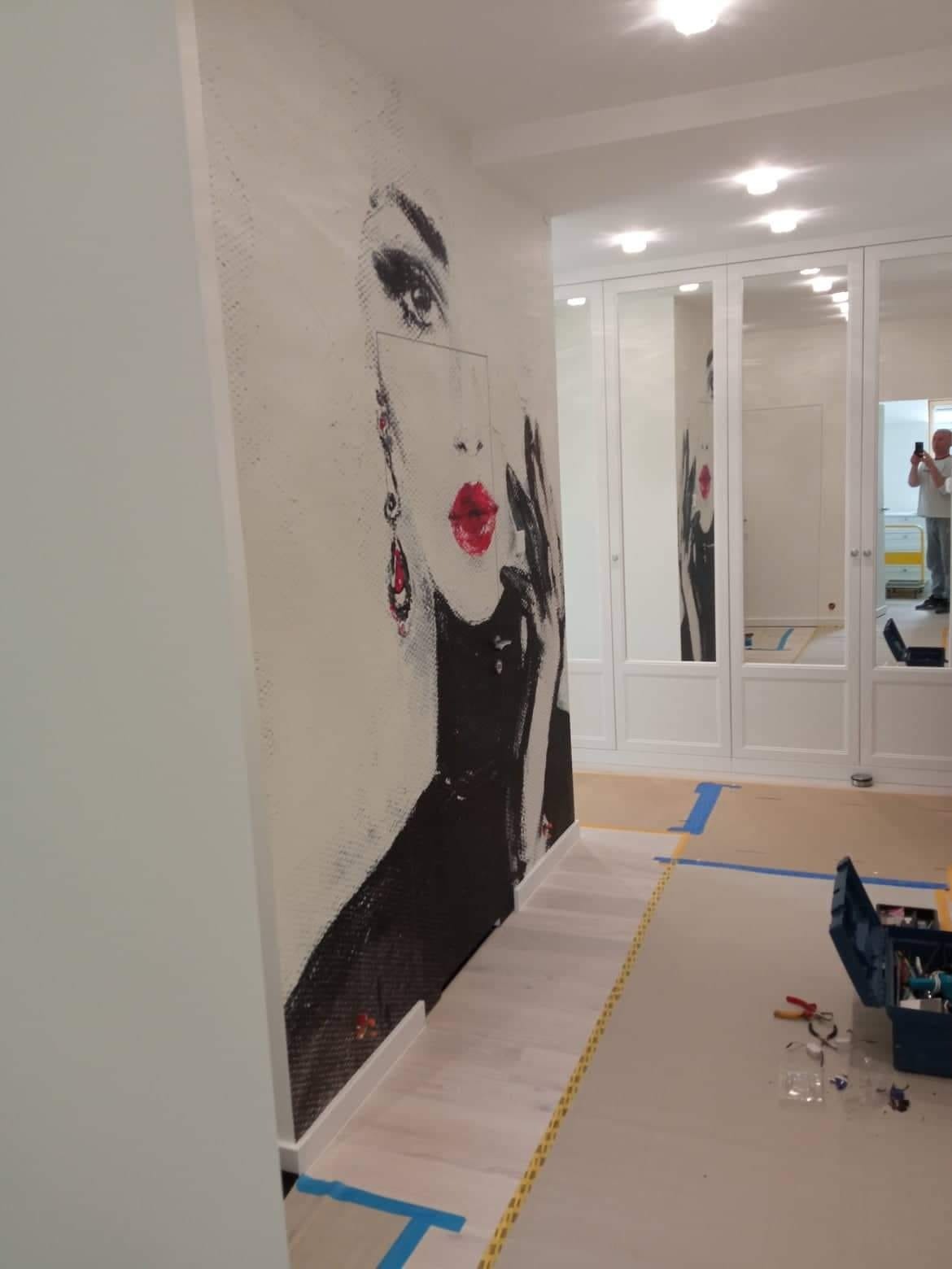 Ściana z fototapetą przedstawiającą portret kobiety w stylu pop-art, widoczne narzędzia i zabezpieczenia podłogi wskazują na prace wykończeniowe.
