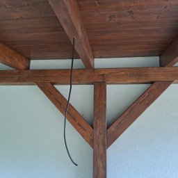 IVAN SHEVCHUK PRO100BUD - Drewniana konstrukcja z belek w kolorze ciemnego brązu, widoczna od dołu, z wystającym kablem elektrycznym i jasną ścianą w tle.