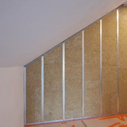 IVAN SHEVCHUK PRO100BUD - Skośna ściana poddasza w trakcie izolacji wełną mineralną, widoczne metalowe profile i zabezpieczona podłoga.