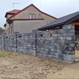 IVAN SHEVCHUK PRO100BUD - Nowoczesny, szary ogrodzenie modułowe z pustaków betonowych, z widocznymi przerwami między elementami, na tle domu z czerwoną dachówką i drewnianej wiaty.