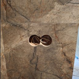 IVAN SHEVCHUK PRO100BUD - Fragment ściany wyłożonej płytami imitującymi marmur, z dwoma okrągłymi otworami na kable elektryczne.