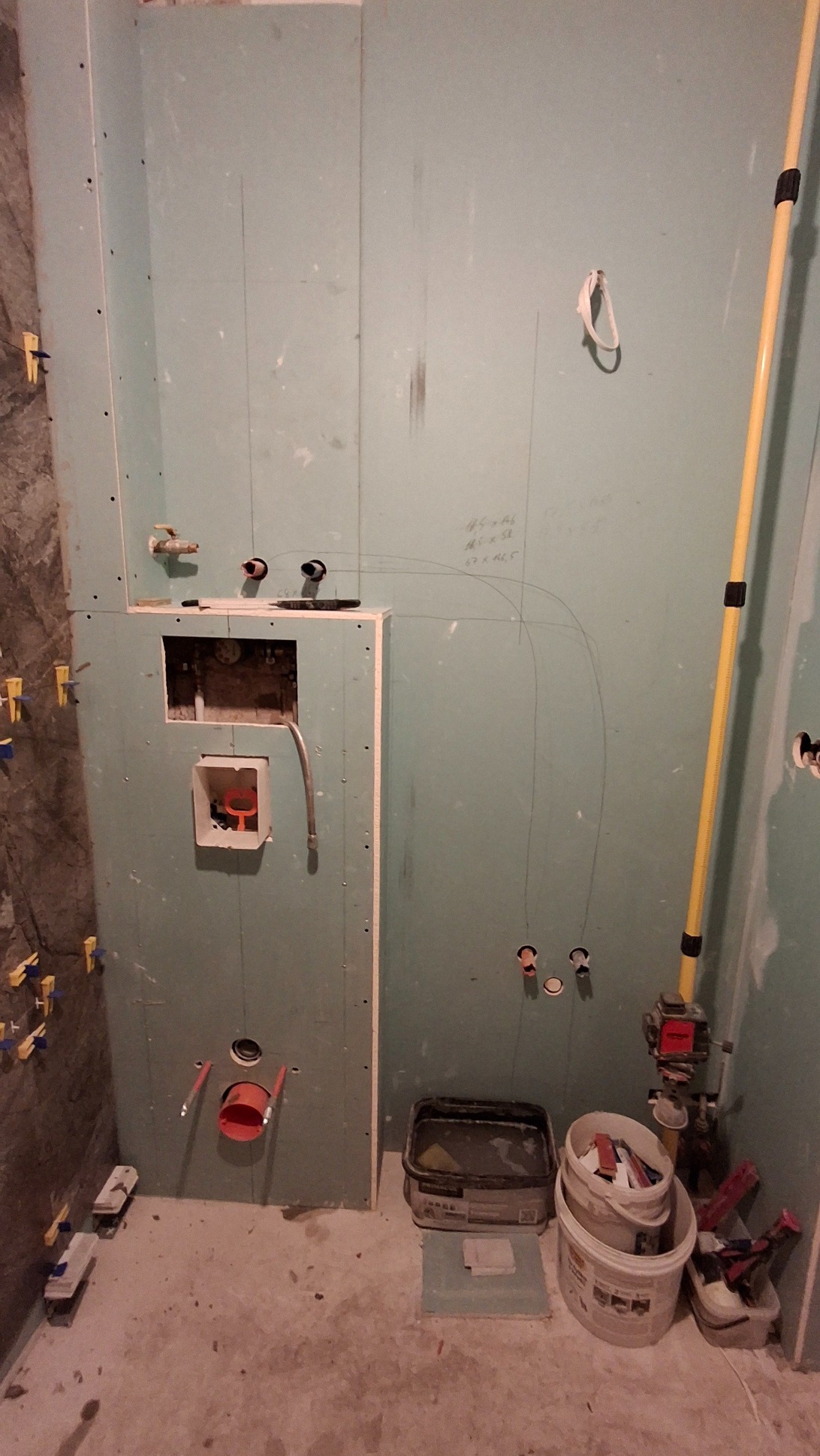 Łazienka w trakcie przygotowania do położenia płytek, widoczne płyty gipsowo-kartonowe, wyznaczone punkty instalacji, poziomica laserowa i akcesoria glazurnicze.