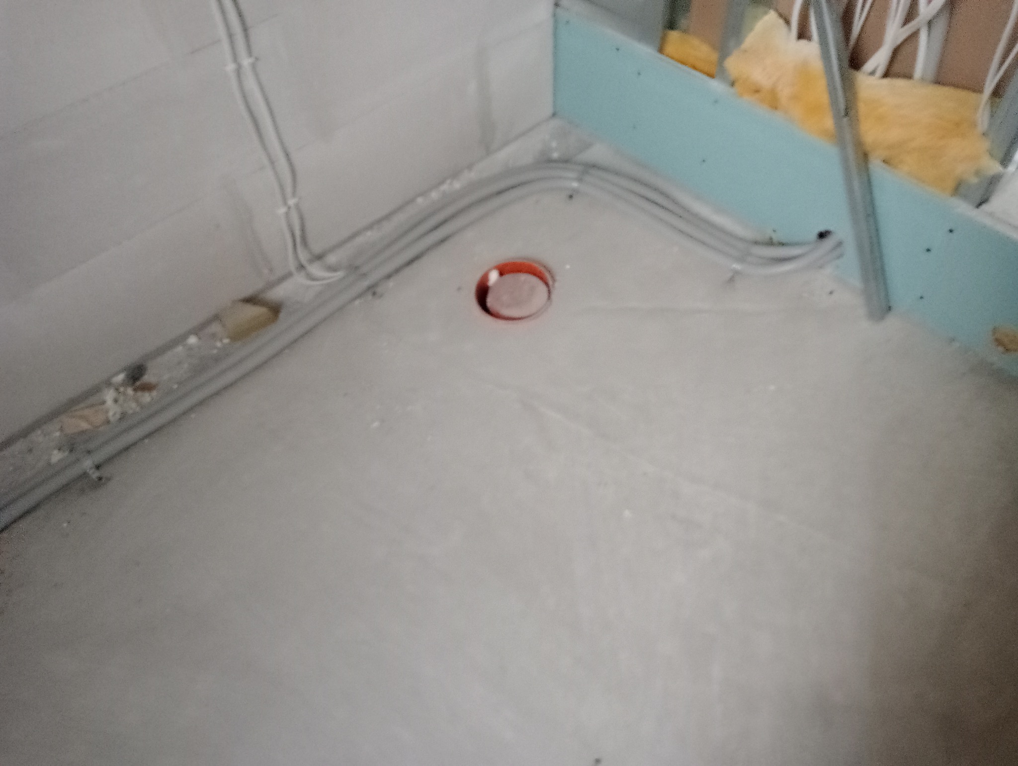 Szare kable elektryczne prowadzone wzdłuż ściany i podłogi w surowym wnętrzu, widoczne puszki instalacyjne i fragment konstrukcji ściany działowej z wełną mineralną.