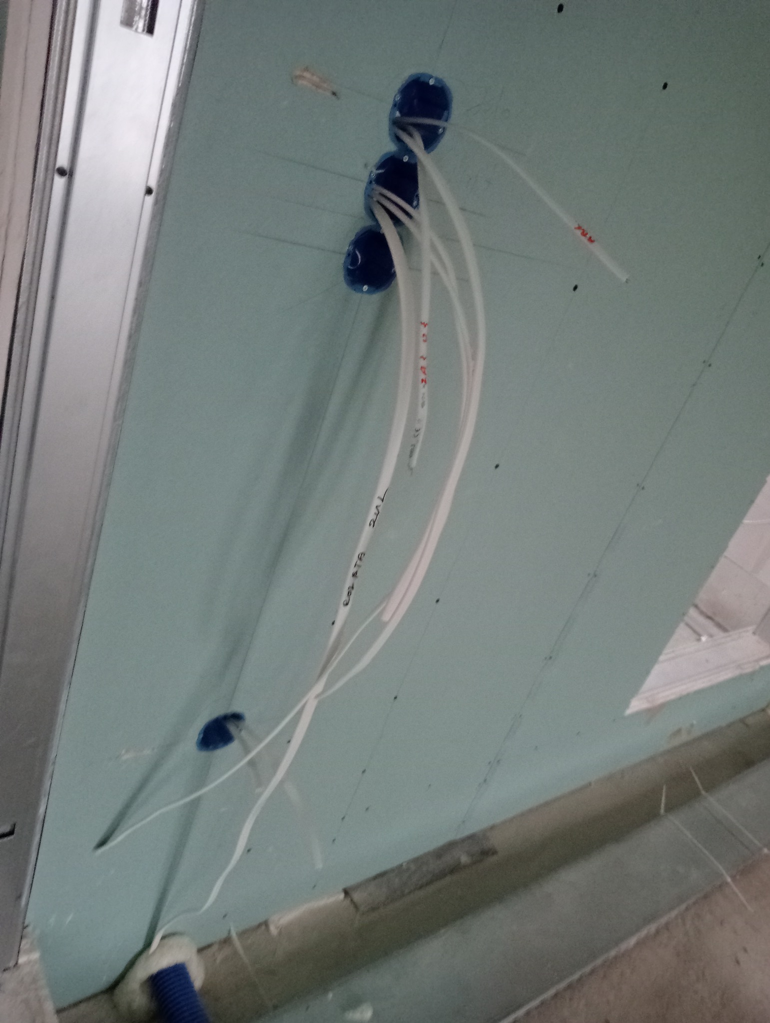 Niebieskie puszki elektryczne podtynkowe zamontowane w płycie gipsowo-kartonowej z wystającymi przewodami z nadrukowanymi oznaczeniami.