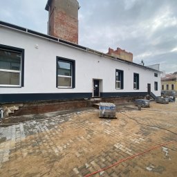 West Bud Ivan Shubak - Budynek po remoncie elewacji z widocznymi paletami kostki brukowej na placu, przygotowanym do ułożenia.