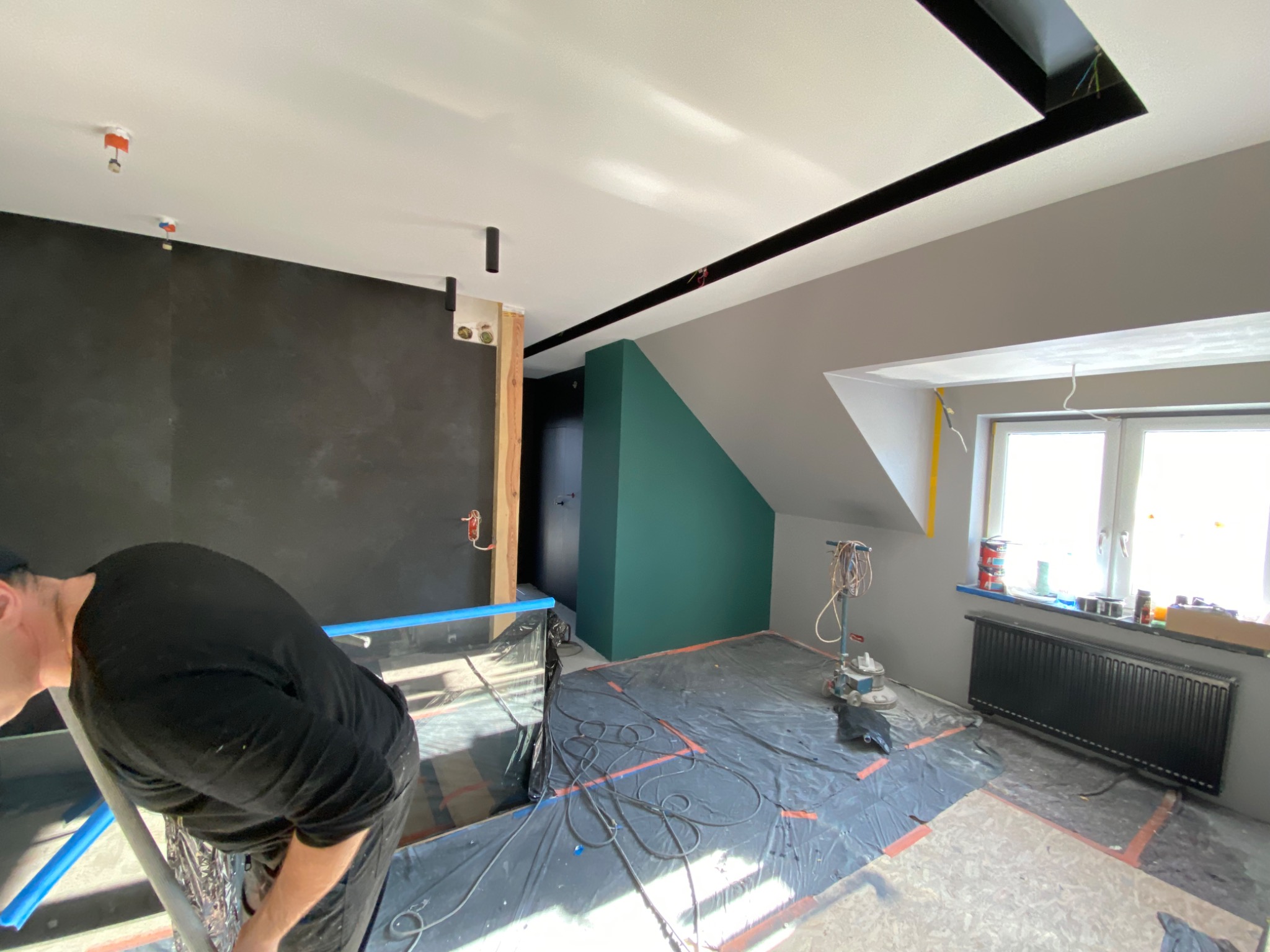 Prace wykończeniowe w pokoju na poddaszu: przygotowanie podłoża pod gładzie, widoczna maszyna do szlifowania, zabezpieczona folią podłoga, pomalowane ściany w różnych kolorach.