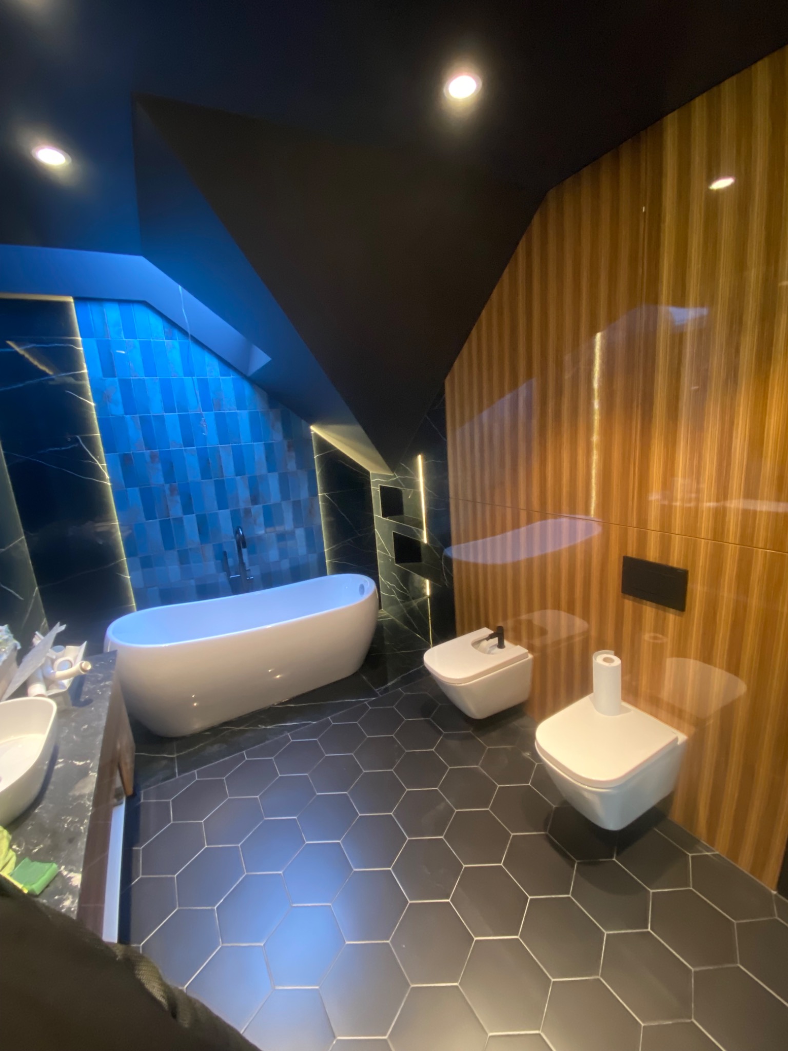 Nowoczesna łazienka z niebieskimi płytkami w pionowy wzór, wolnostojącą wanną, drewnianą ścianą i heksagonalną podłogą