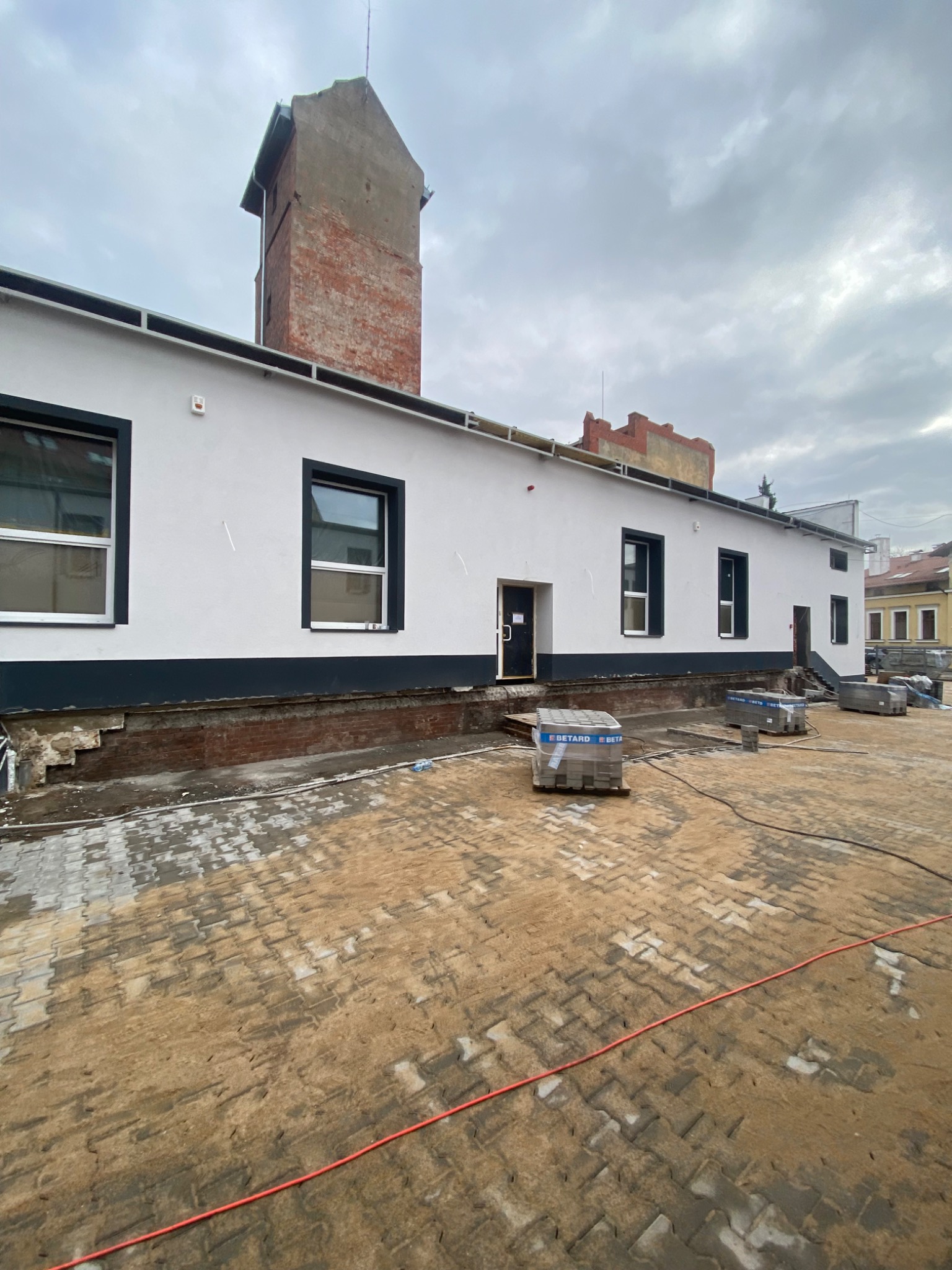 Budynek po remoncie elewacji z widocznymi paletami kostki brukowej na placu, przygotowanym do ułożenia.