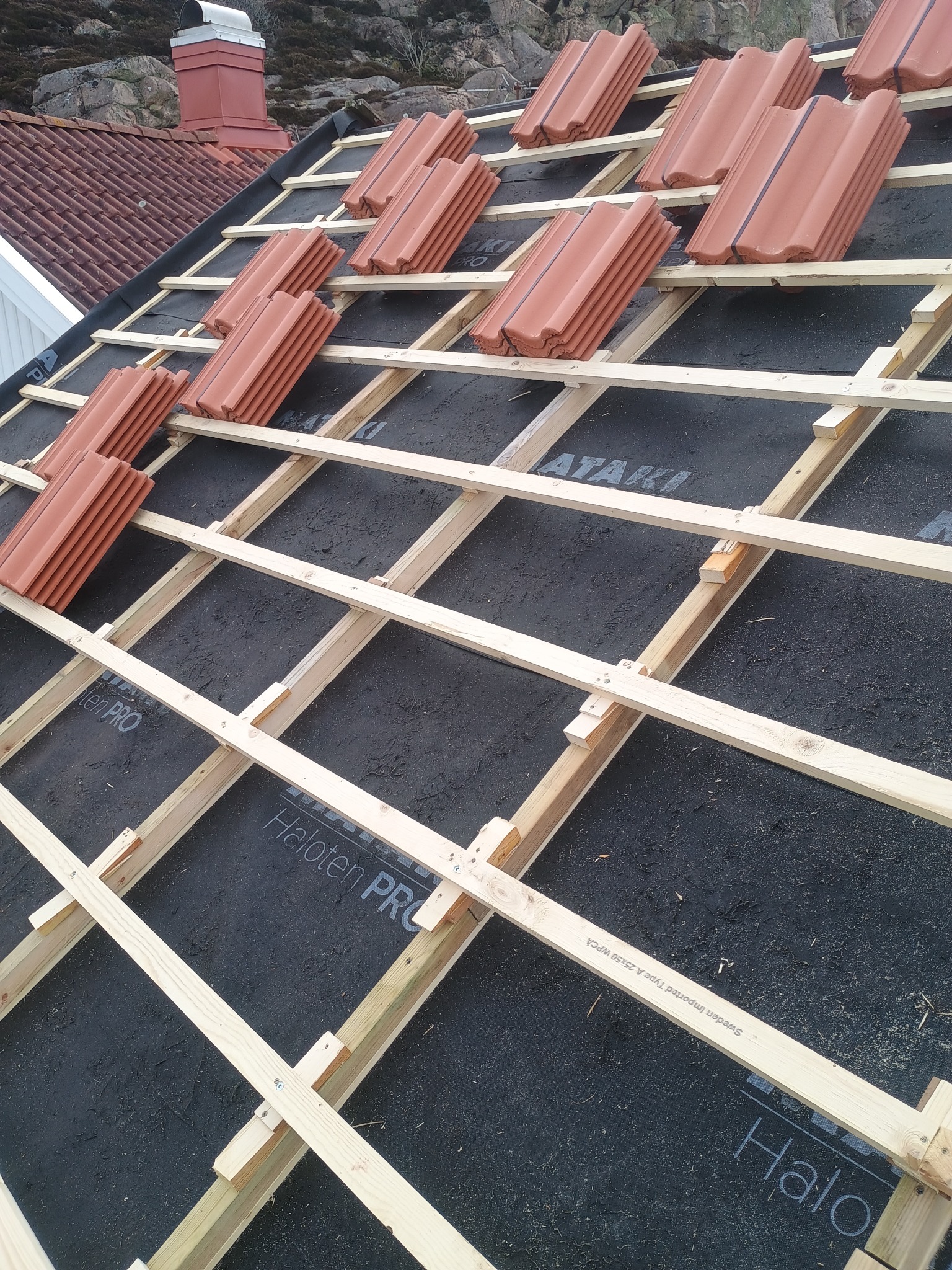 Konstrukcja drewniana dachu z membraną i ułożonymi w stosy dachówkami ceramicznymi przed właściwym kryciem, widok z góry.