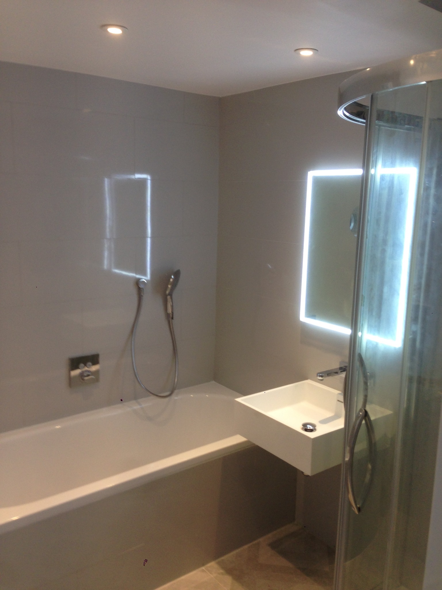 Nowoczesna łazienka z wanną, podświetlanym lustrem i kabiną prysznicową z widocznym uchwytem, wykończona w szarej kolorystyce.