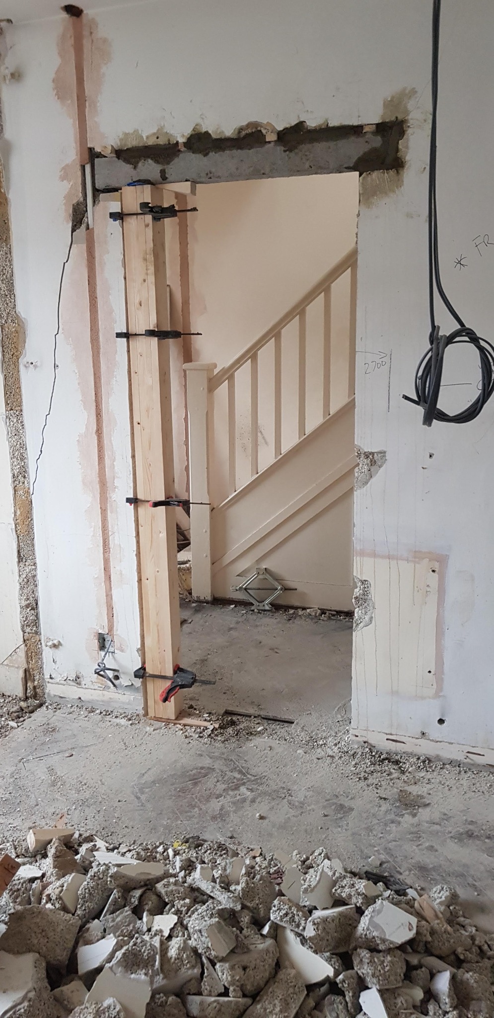 Przygotowanie otworu drzwiowego w Białymstoku: wzmocnienie drewnianą konstrukcją z użyciem zacisków stolarskich, widoczne gruz i uszkodzenia ścian.