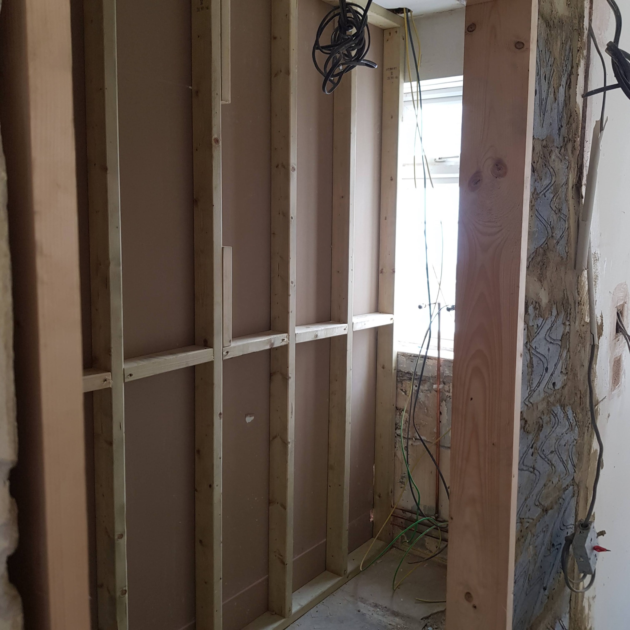 Konstrukcja szkieletowa z drewnianych belek, częściowo obłożona płytą, widoczne przewody elektryczne i fragment ściany z resztkami starego tynku