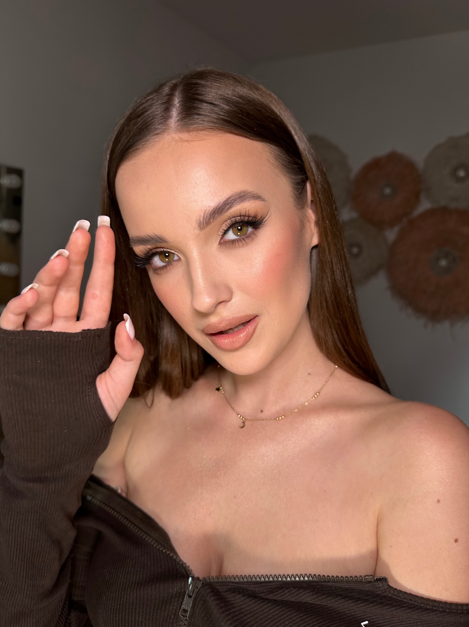 Portret kobiety z profesjonalnym, wieczorowym make-up'em, w tym sztuczne rzęsy i delikatny konturing, pozującej z dłonią uniesioną przy twarzy, prezentując manicure hybrydowy.