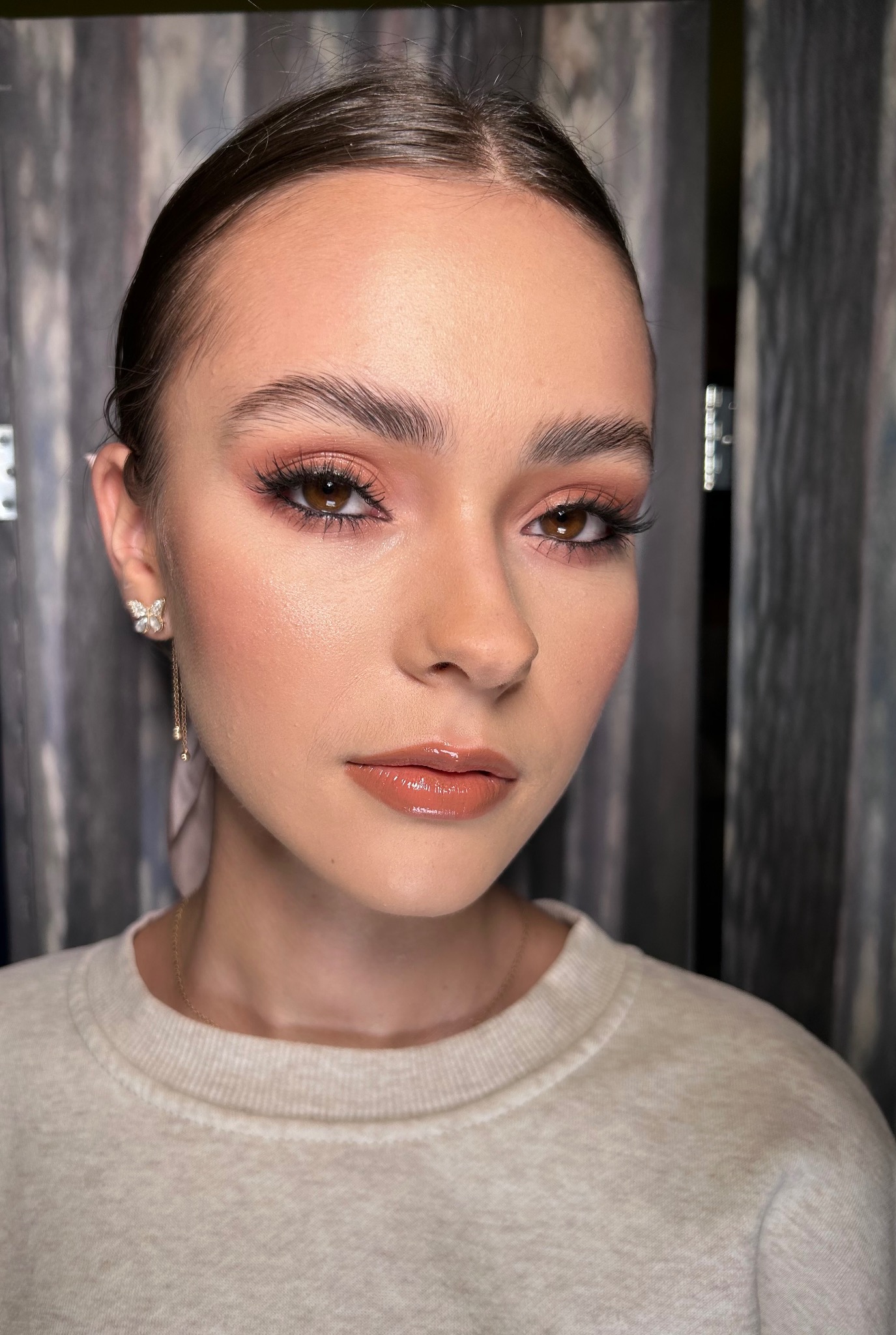 Portret kobiety z delikatnym, brzoskwiniowym makijażem oczu i błyszczącymi ustami w Nowym Targu, z widocznym kolczykiem w kształcie motyla.