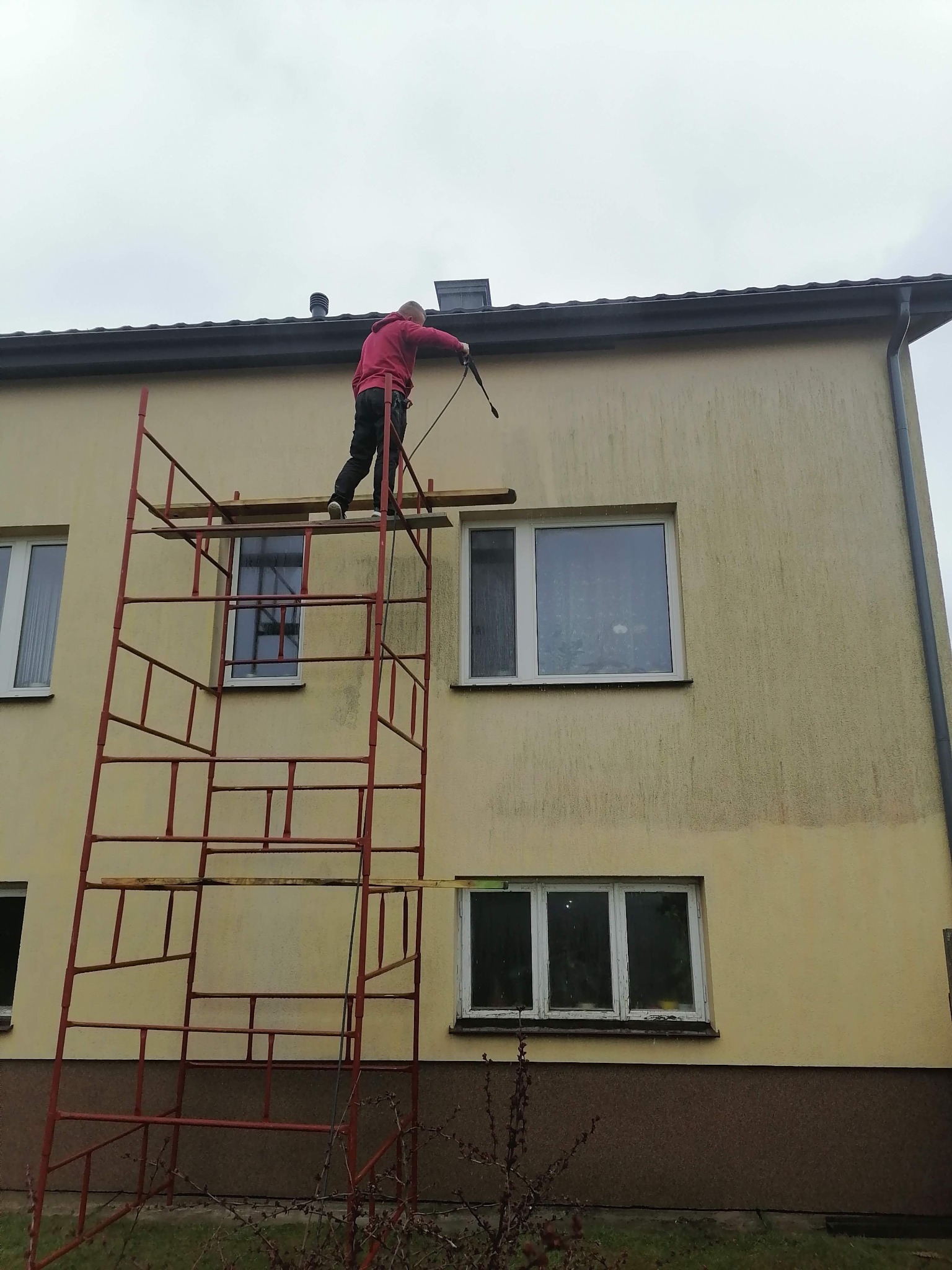 Pracownik na rusztowaniu w Lublinie czyści elewację budynku za pomocą myjki ciśnieniowej, przygotowując ją do malowania.