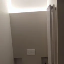 Nowoczesna, minimalistyczna toaleta w odcieniach szarości, z podwieszaną miską WC, ukrytym oświetleniem sufitowym i grzejnikiem drabinkowym.