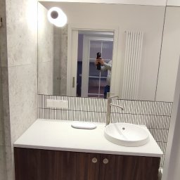 Wojciech Dutkiewicz - Nowoczesna łazienka z umywalką nablatową, szafką z ciemnego drewna i dużym lustrem, w którym odbija się osoba robiąca zdjęcie telefonem.