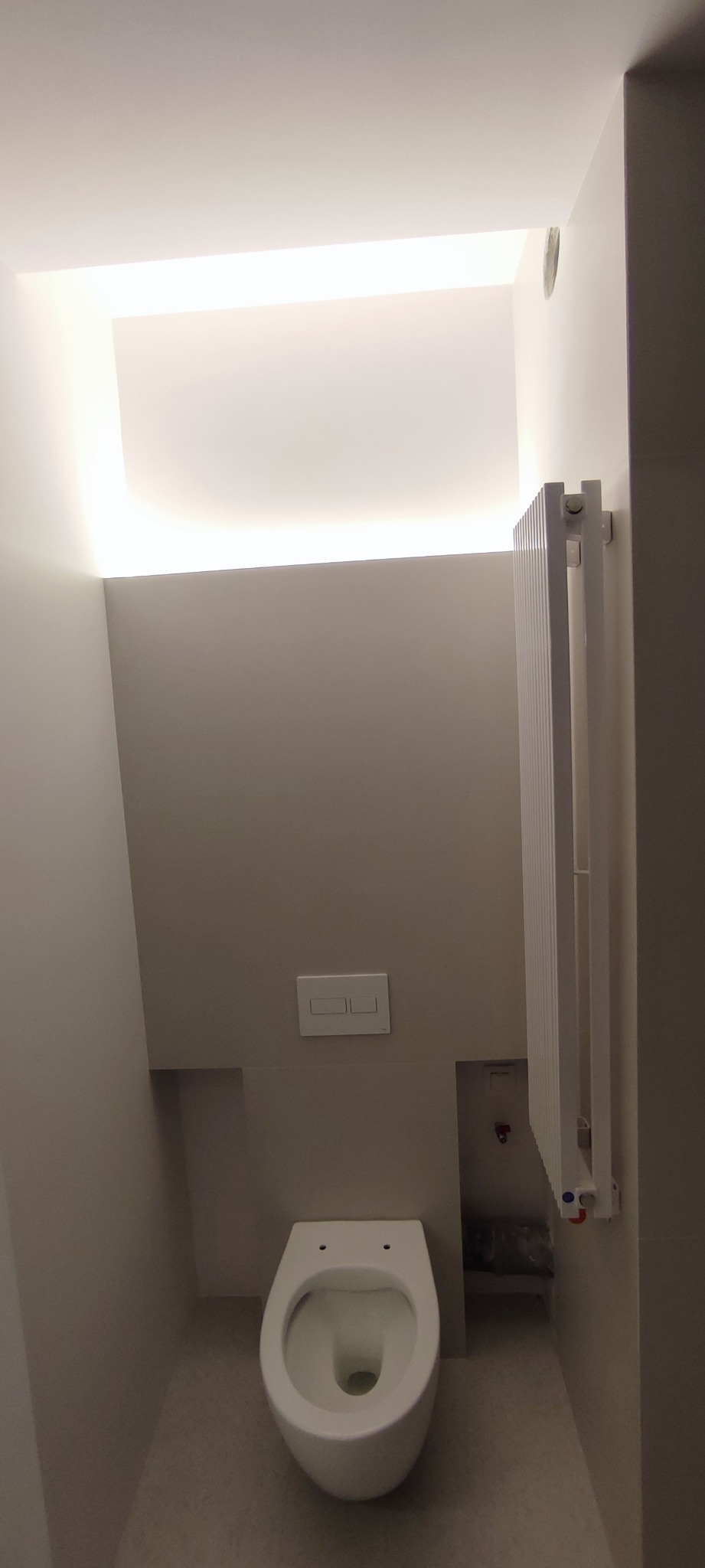 Nowoczesna, minimalistyczna toaleta w odcieniach szarości, z podwieszaną miską WC, ukrytym oświetleniem sufitowym i grzejnikiem drabinkowym.