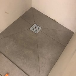 Firma Budowlana Tomasz Jędroszka - Ułożona podłoga w kabinie prysznicowej z odpływem liniowym w centralnej części i pomarańczowym krzyżykiem dystansowym.